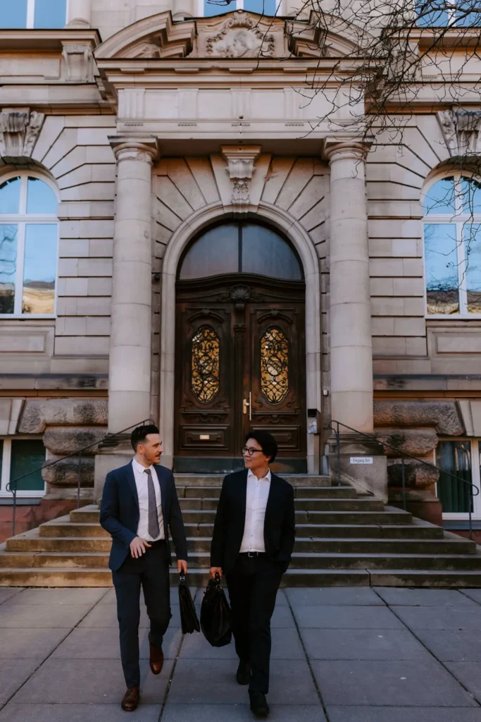 Die Rechtsanwälte Maximilian Schüßler und Xiao Zhang laufen vor dem Eingang eines historischen Gebäude.